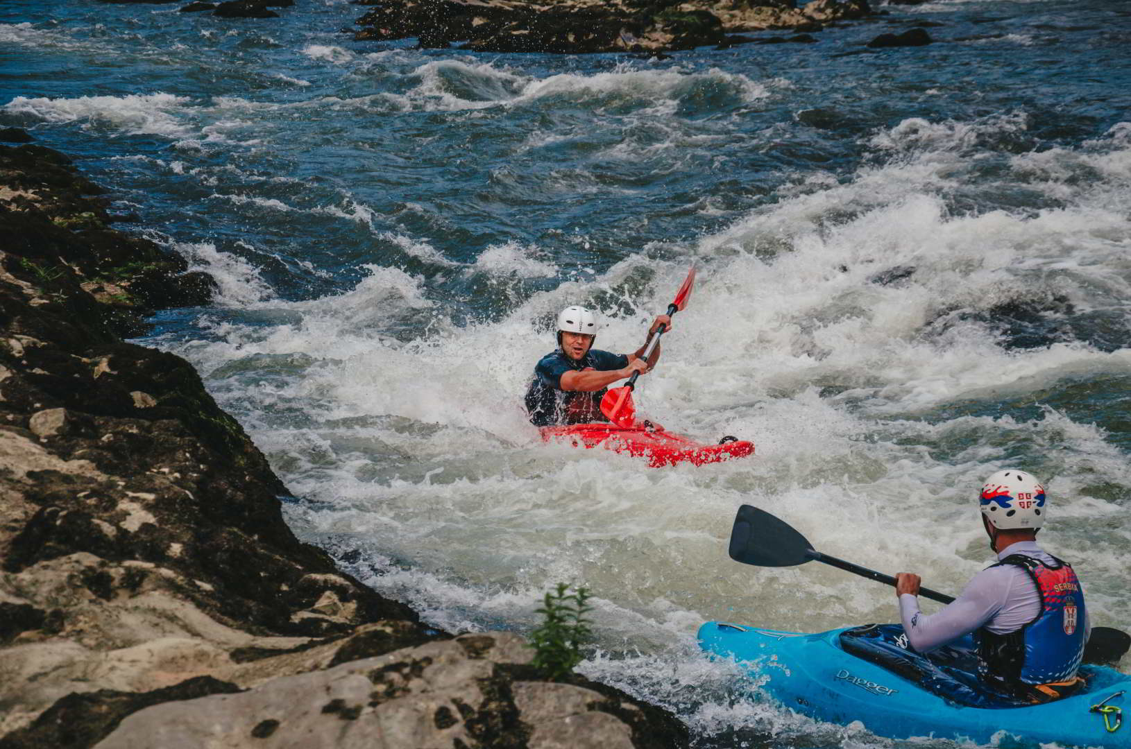 Two men are kayaking on the river in the rapids