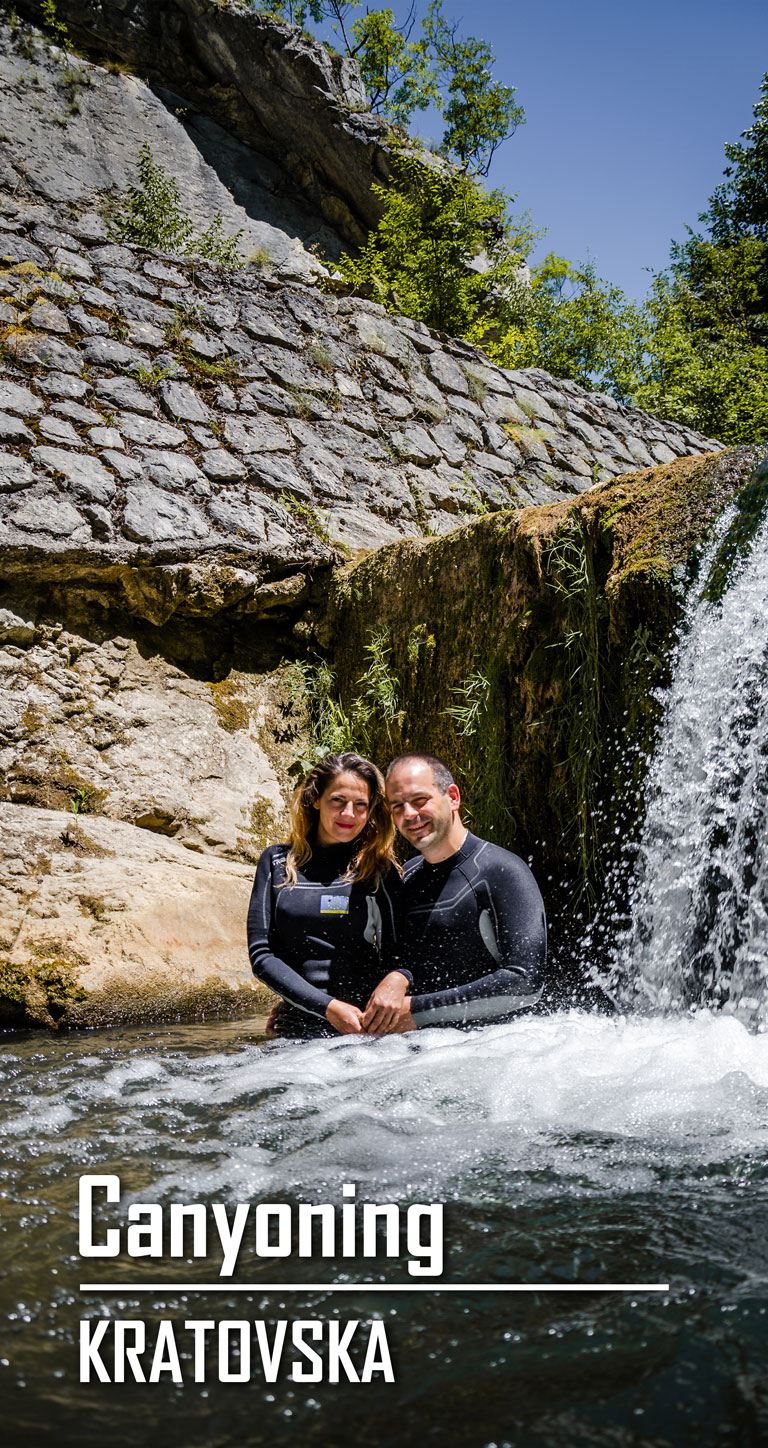A man and a woman are standing beneath a waterfall