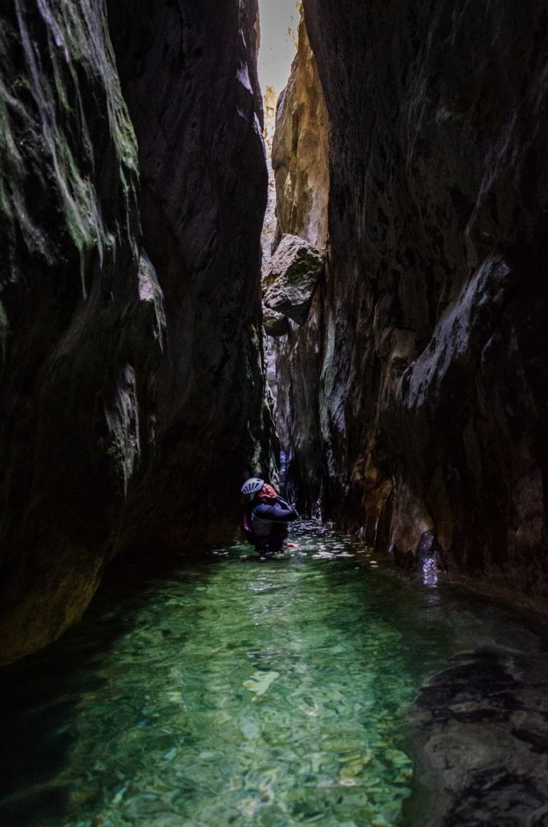 Muškarac stoji u čisto zelenoj vodi koja teče kroz kanjon